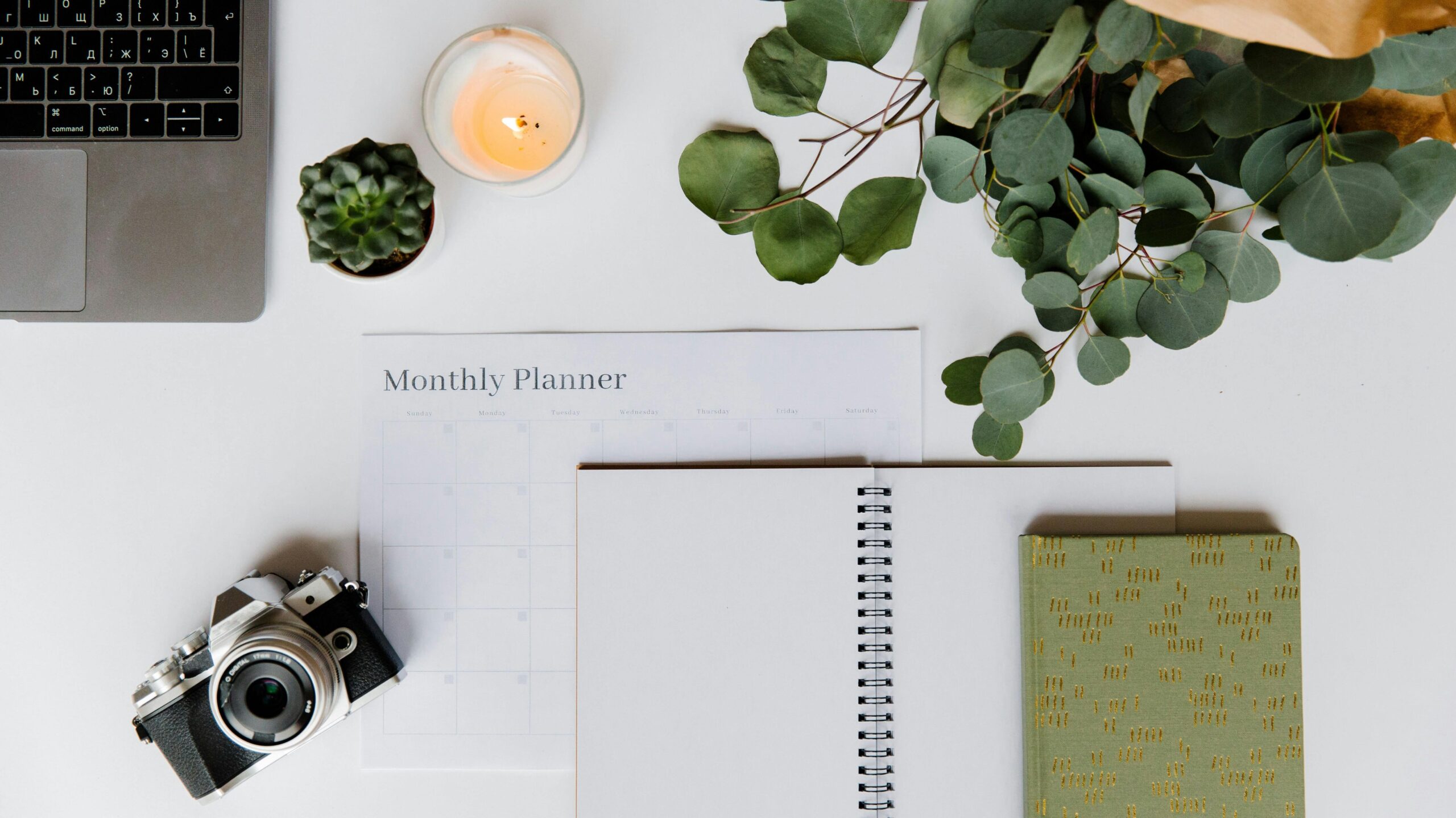 Flat lay of a creative workspace with a planner, analog camera, and laptop for inspiration.